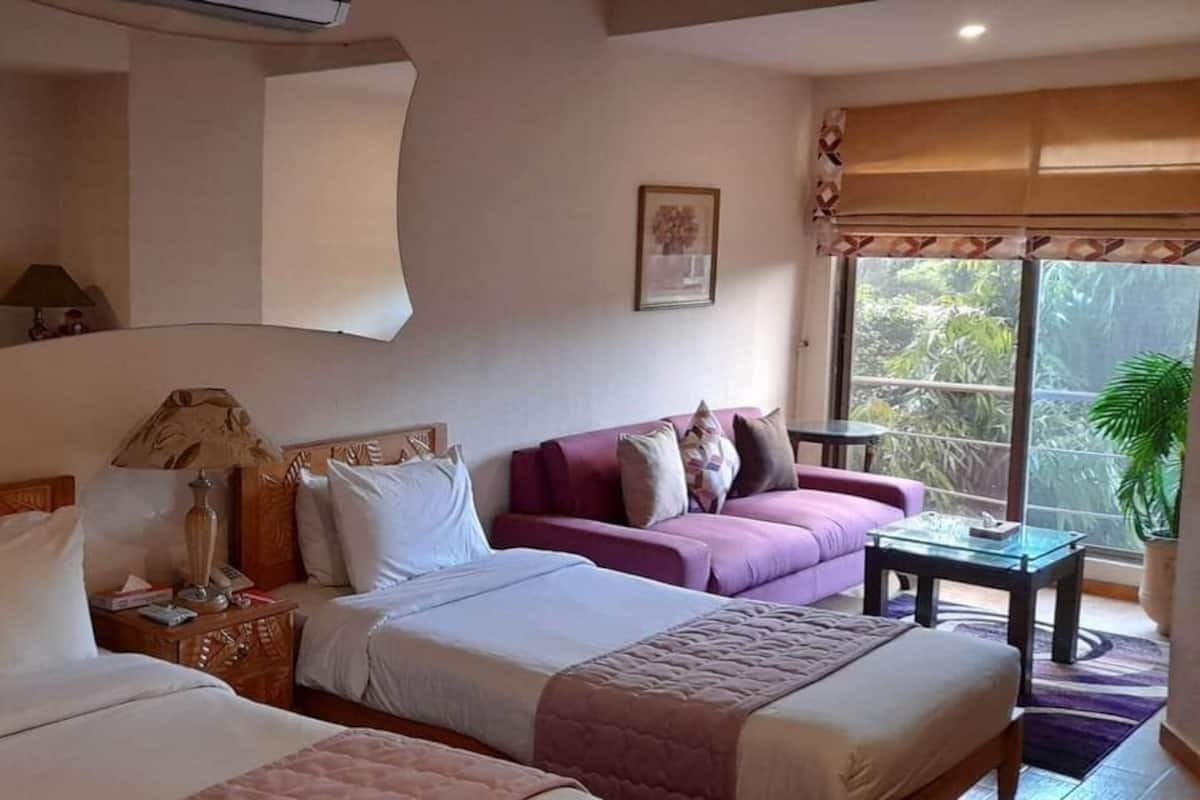 Een hotelkamer met twee bedden, een bank, een klein tafeltje en een raam met uitzicht op groen.