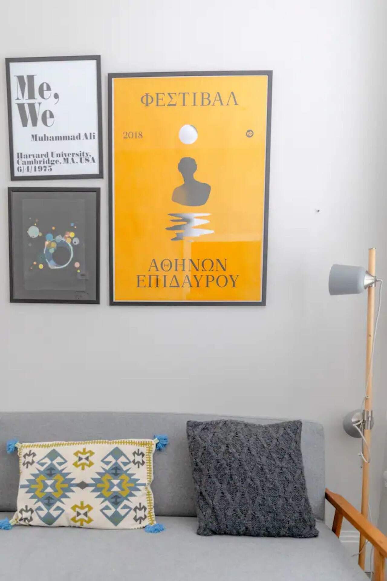A room with a grey sofa, a patterned throw pillow, and a framed poster on the wall.