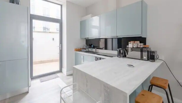 Una cocina moderna con una isla grande, armarios azul claro y un portón corredizo de vidrio que da a un espacio exterior.