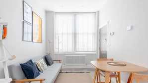 Una sala de estar moderna con un sofá gris, una mesa de comedor de madera y un gran ventanal con persianas.