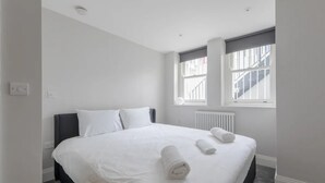 Moderni hotellihuone, jossa on suuri sänky, valkoiset vuodevaatteet ja kaksi rullalle taitettua pyyhettä.
