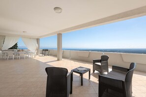 A covered outdoor area with a dining table and chairs, a small table with a book, and a view of the sea. - 3499 Villetta Panorama by Barbarhouse (Fasano)