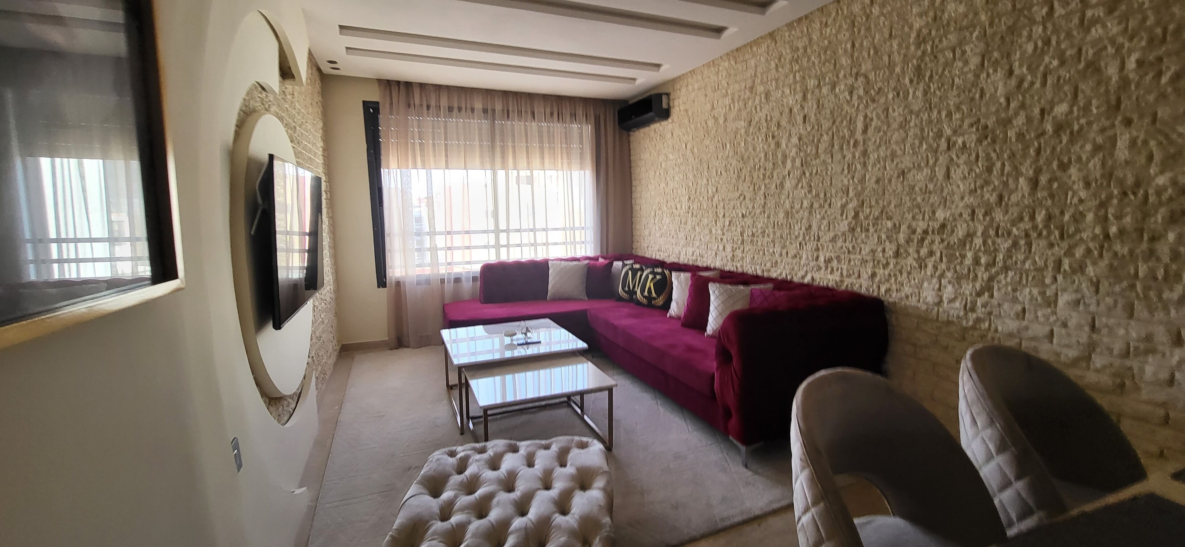 A living room with a sofa, a glass coffee table, and a television mounted on the wall.