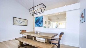 A dining area with a wooden table and benches, a hanging light fixture, and artwork on the walls. - One More Day (Sanibel)