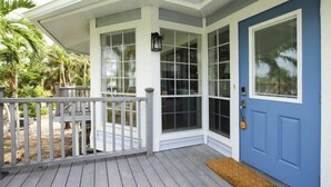 A covered porch with a blue door, white railings, and a small rug. - One More Day (Sanibel)