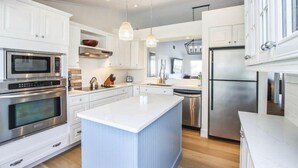 A modern kitchen with white cabinetry, stainless steel appliances, and a central island. - One More Day (Sanibel)