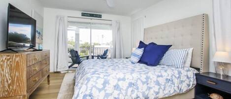 A bedroom with a large bed, a TV, a ceiling fan, a dresser, and a balcony with a view.