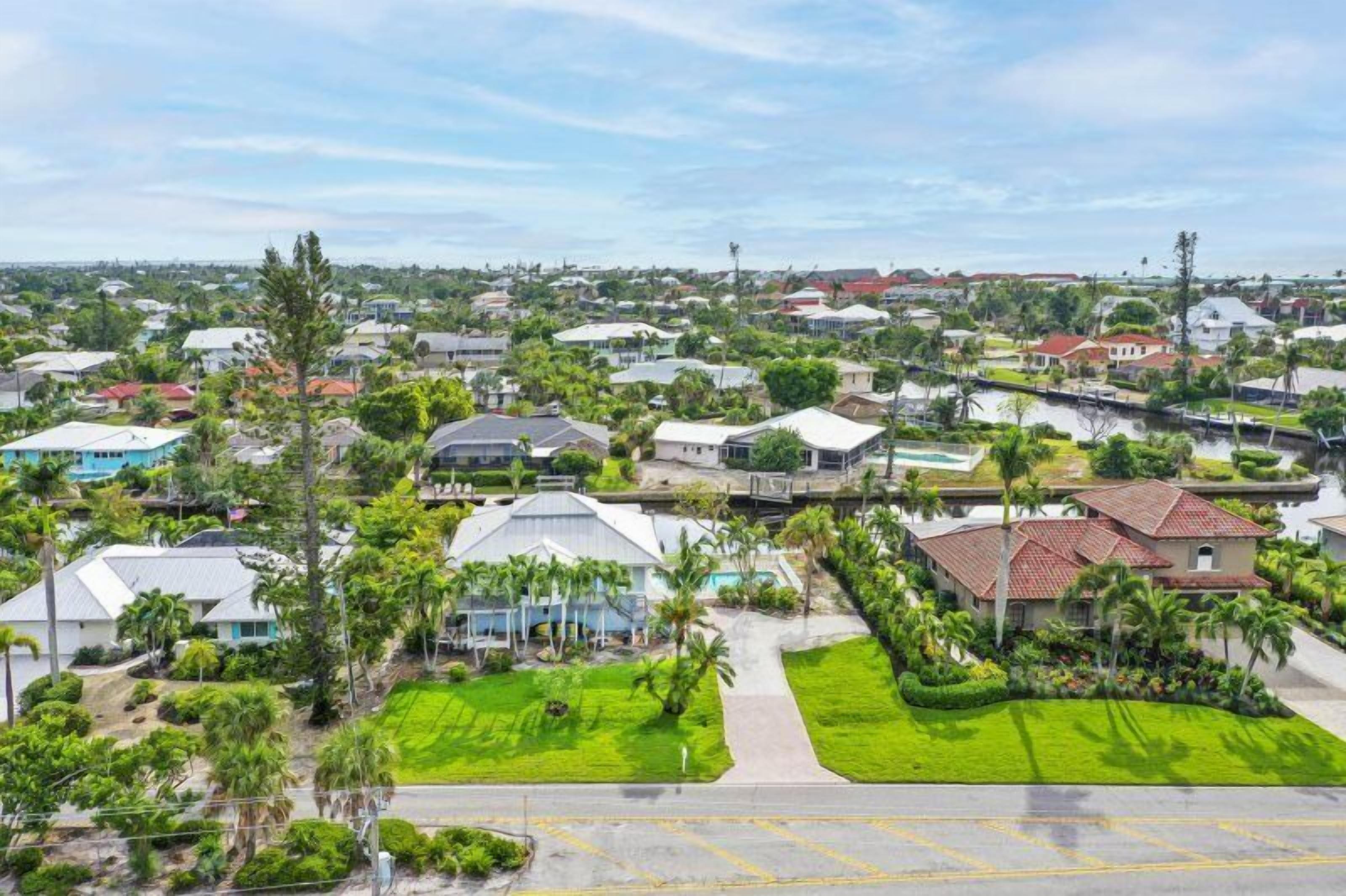 A residential area with houses, green lawns, and palm trees.
