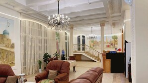 A spacious living room with a chandelier, leather sofas, a dining area, and a staircase leading to an upper level. - Prestige Terrace Hotel (Bukhara)