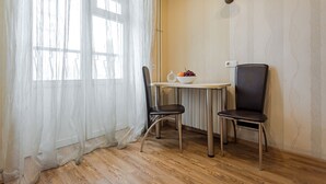 A room with a wooden floor, a table with chairs, a bowl of fruit, and a wall-mounted light fixture. - Stylish apartment near the railway station (Minsk)