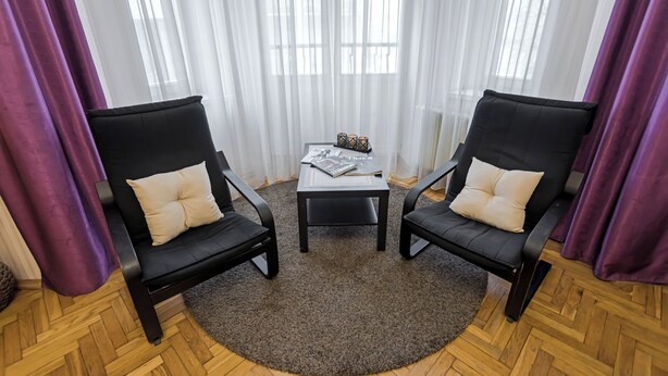 A room with two black leather chairs, a small table with a magazine, and a window with sheer white curtains. - Stylish apartment near the railway station (Minsk)
