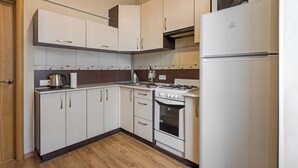 A compact kitchen with white cabinets, a stove, a microwave, and a refrigerator. - Stylish apartment near the railway station (Minsk)