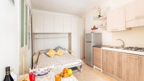 Un dormitorio pequeño con cama, mesita de noche y una kitchenette con refrigerador y lavaplatos.