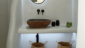 Ein Badezimmer mit einem weißen Waschbecken, einem Spiegel, zwei schwarzen Seifenspendern und zwei gewebten Körben.