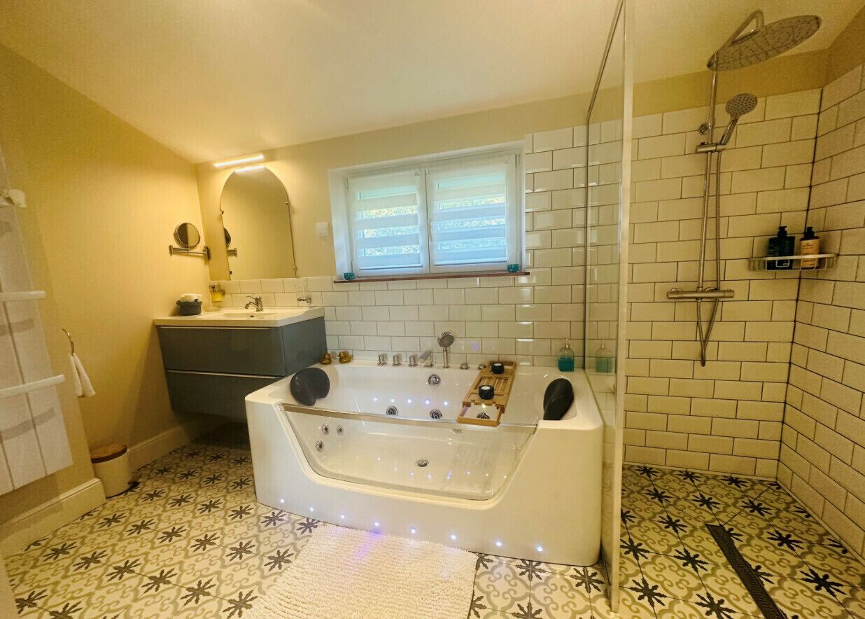 A bathroom with a large bathtub, a shower, and a window with blinds.