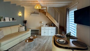 A spacious living area with a high ceiling, a wooden staircase, a sofa, a dining table with chairs, and a TV mounted on the wall. - Au domaine du Pré Dieu (Crécy-sur-Serre)