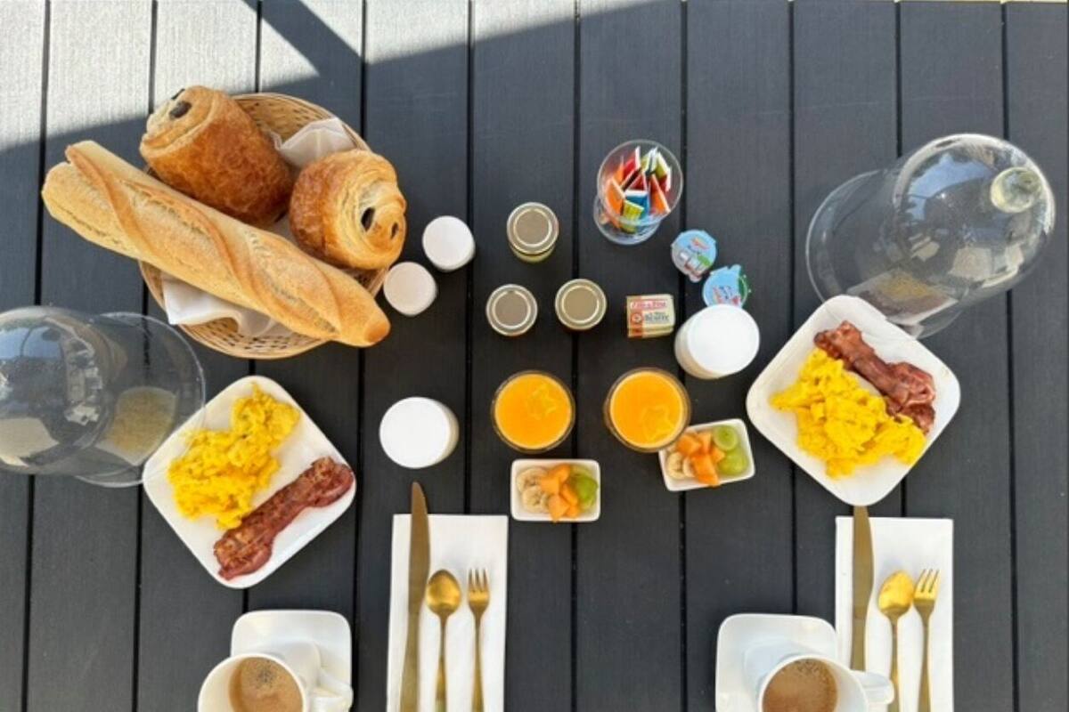 Une table de petit-déjeuner avec des croissants, des œufs brouillés, du bacon, du jus d’orange et du café.