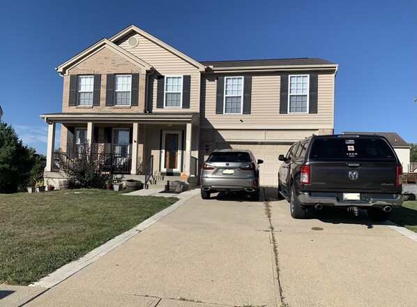 A two-story house with a front porch, a garage, and two parked vehicles. - Cincinnati/KY Airport-5Bed Vacation Home-close to Cincinnati, Ark, I71/75 (Florence)
