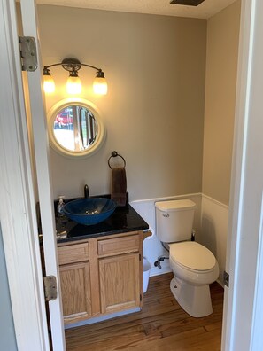A small bathroom with a wooden vanity, a round mirror, a blue sink, and a toilet. - Cincinnati/KY Airport-5Bed Vacation Home-close to Cincinnati, Ark, I71/75 (Florence)