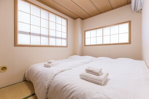 A hotel room with two beds, large windows, a ceiling fan, and a wall-mounted air conditioner. - Tatekawa 333 Residence (Tokyo)