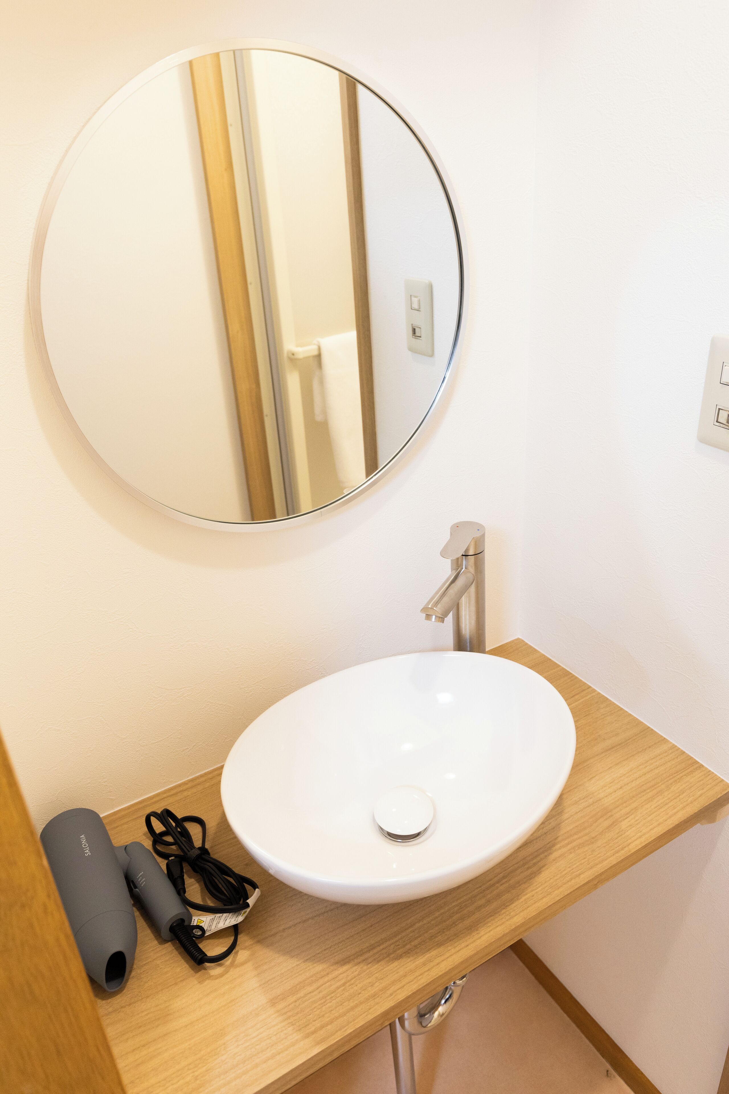 A bathroom with a round mirror, a white sink, and a hairdryer on the counter.