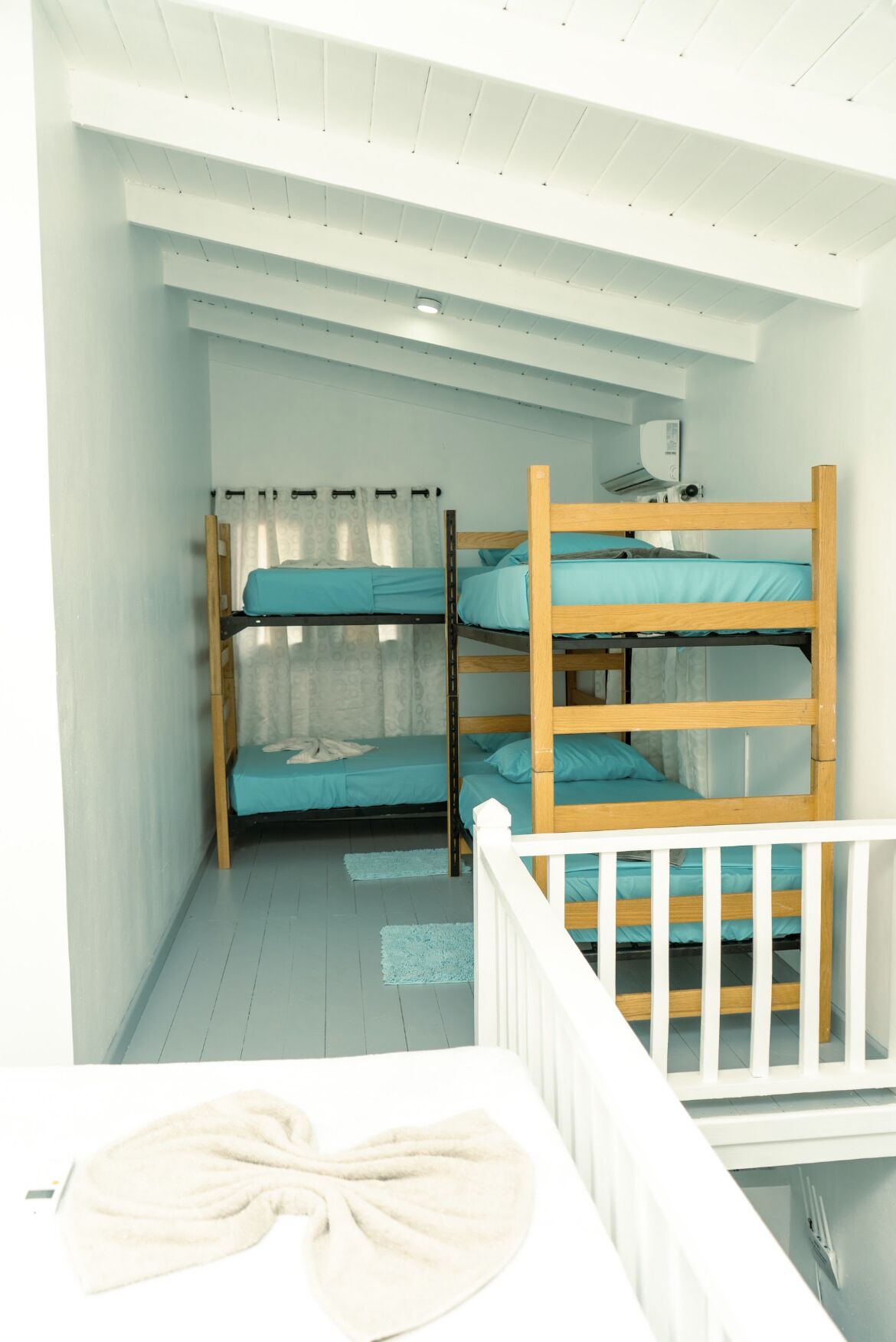 Habitación pequeña con literas, una cuna blanca y un ventanal con cortinas.