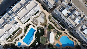 An aerial view of a modern hotel complex with multiple swimming pools, landscaped gardens, and a central circular plaza. - Denia apartment Marina Real III T (Denia)