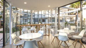 A modern indoor dining area with glass walls, white round tables, and light grey chairs. - Denia apartment Marina Real III T (Denia)