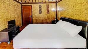 Una habitación con una cama grande, un televisor sobre un mueble bajo, una puerta de madera y un muro con diseños tejidos.