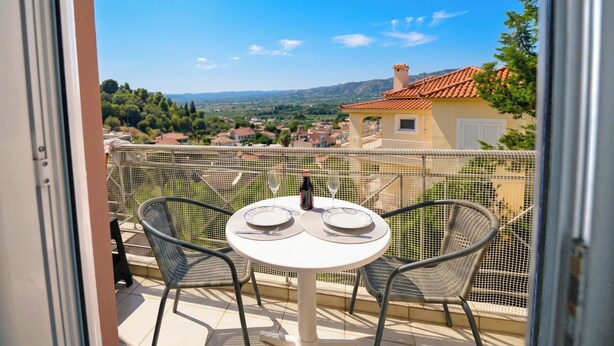Un balcon avec une table dress ée pour deux personnes, une chaise et une vue sur un village.