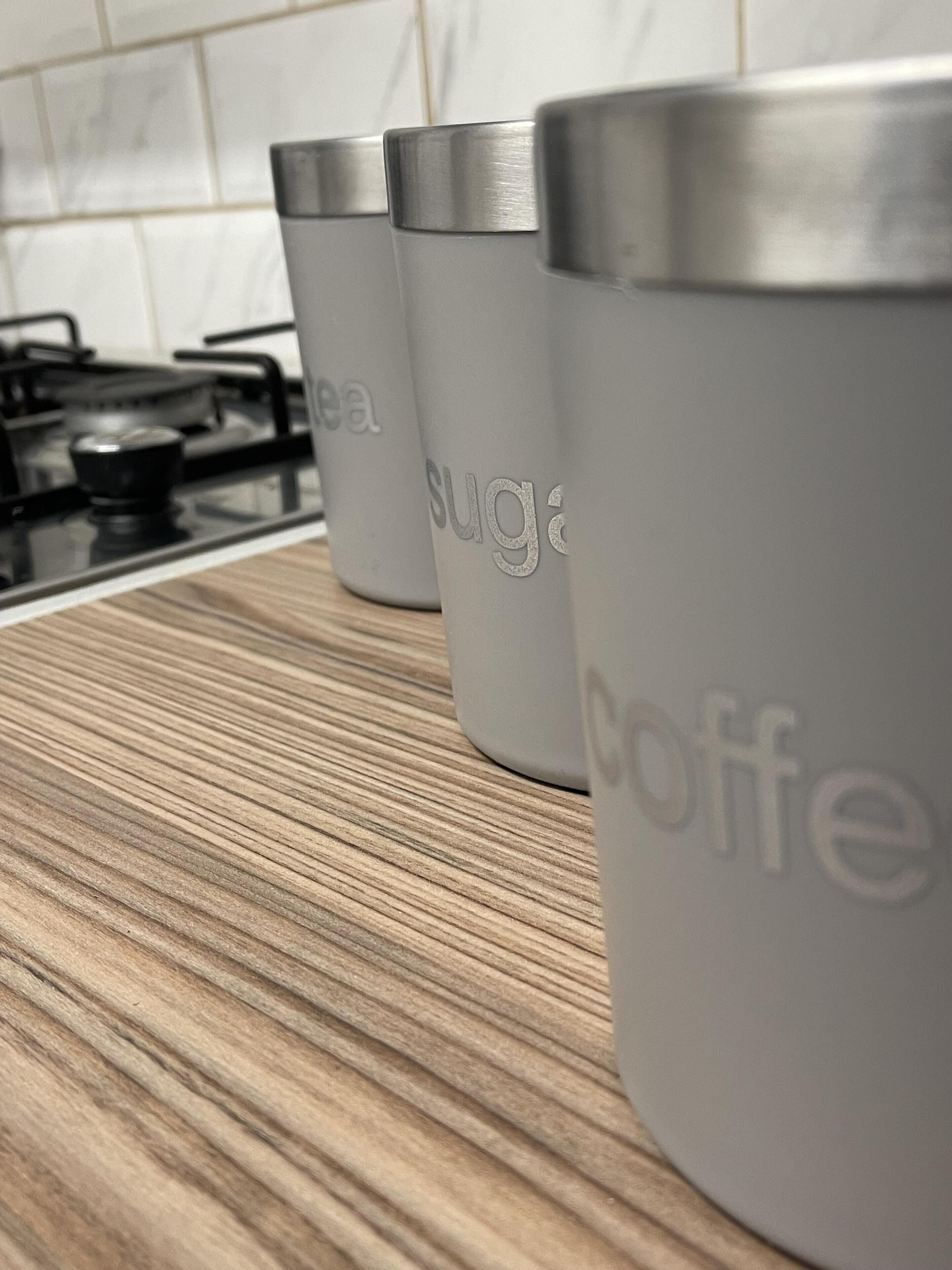 Three stainless steel containers labeled "tea," "sugar," and "coffee" on a kitchen counter.