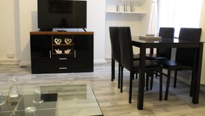 Ett modernt vardagsrum med en platt-TV på ett trästativ, ett bord i glas och en matplats med ett svart bord och stolar.
