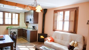 A cozy living room with a sofa, a coffee table, and a fireplace. There is a kitchen area with cabinets and a stove. - Apartamentos Valdecarzana . Braña el Revellón Senda del oso (TEVERGA-OVIEDO-ASTURIAS)