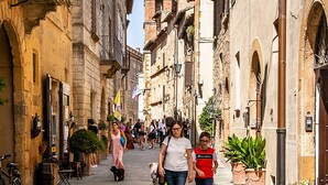 Una calle estrecha flanqueada por edificios históricos, con una torre del reloj a lo lejos y personas caminando.