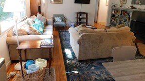 Una sala de estar con sofá, sillón y televisor. Se observa una estantería y una chimenea.