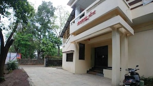 A two-story building with a flat roof and a sign in a foreign language. There is a paved entrance area with a scooter parked outside. - Hotel Matruchhaya Lonavala (Mawal)