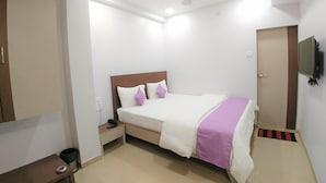 A bedroom with a bed, nightstand, and a television mounted on the wall. - Hotel Matruchhaya Lonavala (Mawal)