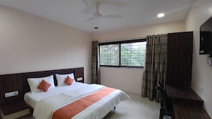A hotel room with a large bed, a desk, a chair, a ceiling fan, and a window with curtains. - Hotel Matruchhaya Lonavala (Mawal)