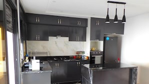 A modern kitchen with dark cabinetry, a central island, a stove, and a refrigerator. - Villa Avec Piscine Privée à Saidia (Saïdia)