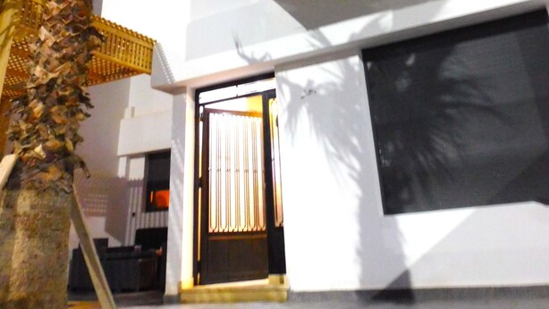 A modern two-story building with a flat roof, a large window, and a door with curtains. - Villa Avec Piscine Privée à Saidia (Saïdia)