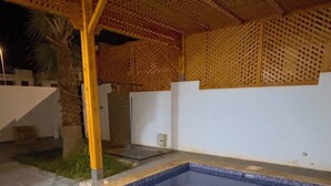 A swimming pool with a blue tiled floor and a wooden pergola overhead. - Villa Avec Piscine Privée à Saidia (Saïdia)
