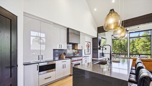 Une cuisine moderne avec des meubles blancs, un îlot central et une grande fenêtre donnant sur les arbres.