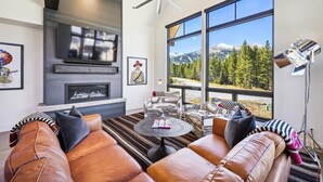 Un salon moderne avec des canapés en cuir, une cheminée, une grande fenêtre donnant sur les montagnes et un ventilateur de plafond.