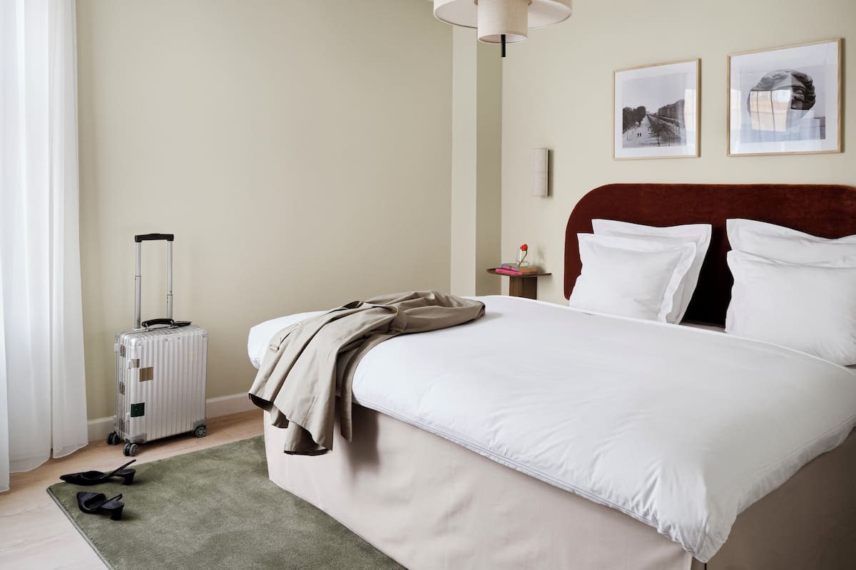 Een keurig opgemaakt hotelkamer met een groot bed, een koffer, een lamp en twee ingelijste foto's aan de muur.