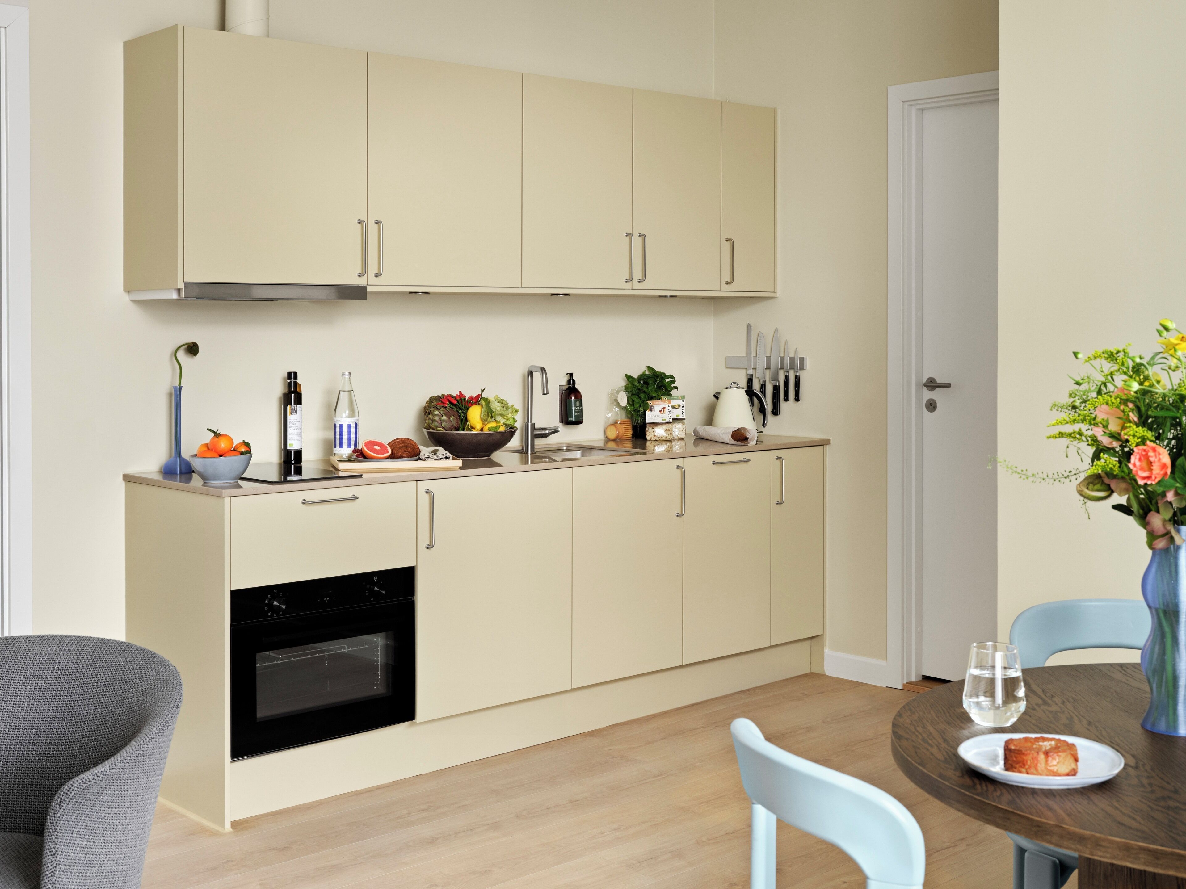 Cocina compacta con horno integrado, una mesa de comedor con sillas y un florero con flores sobre la mesa.