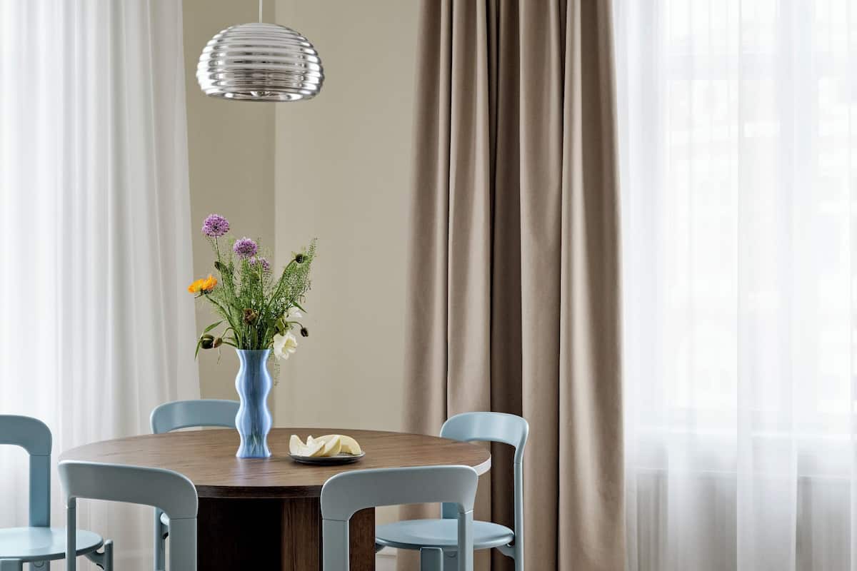 Een eetruimte met een ronde tafel, vier stoelen, een vaas met bloemen en een hanglamp.