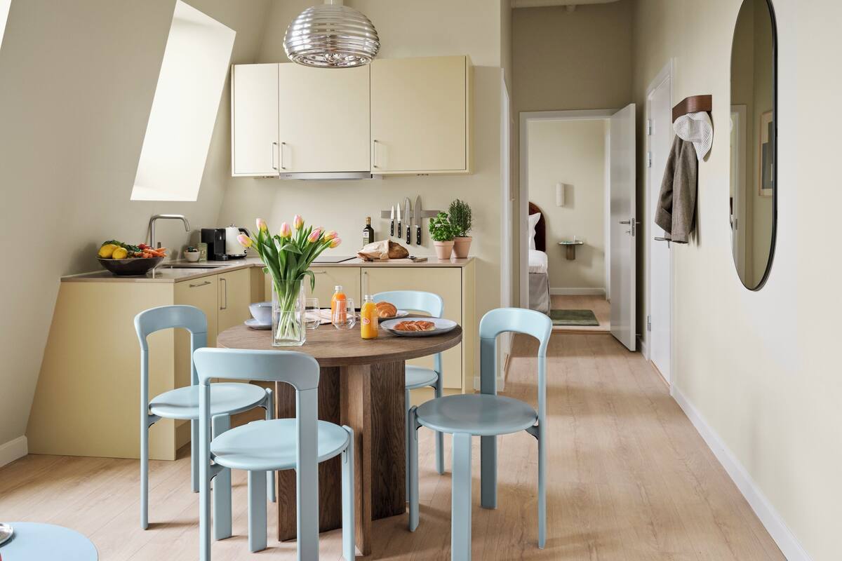 Een moderne keuken met een eethoek, met een ronde houten tafel, lichtblauwe stoelen en een hanglamp.