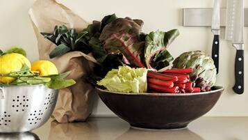 A kitchen counter with a colander, a paper bag, a bowl of mixed vegetables, and two knives.