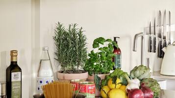 Una cocina con estufa, ollas, un tazón de verduras y una planta en maceta.