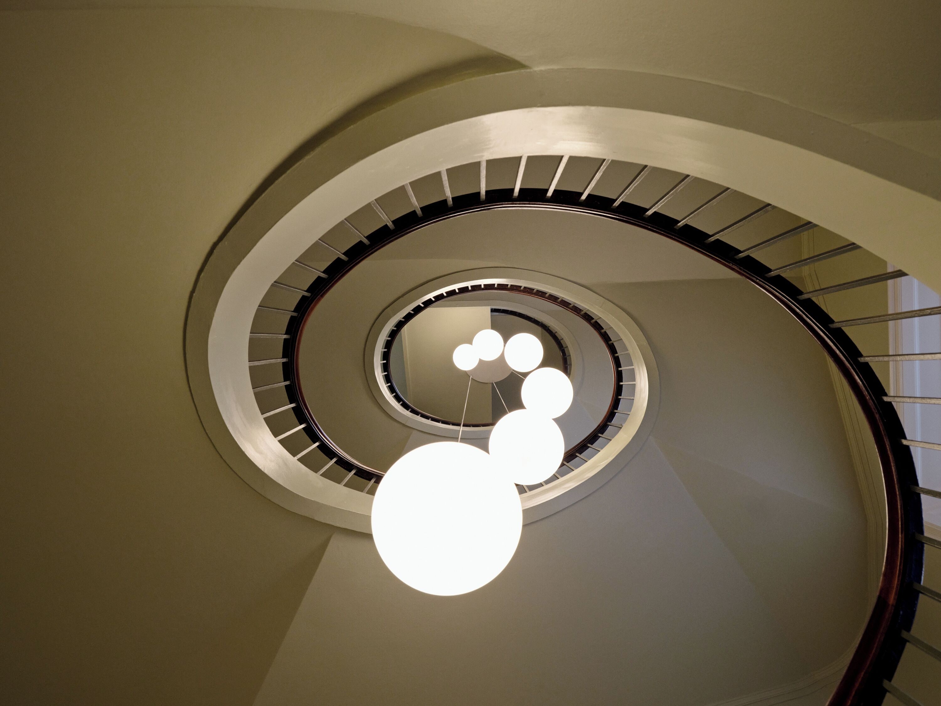 A spiral staircase with a modern design, featuring a central light fixture with multiple spherical elements.